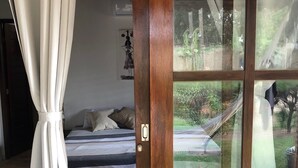 A bedroom with a bed, a window with a view of the outdoors, and a door with a wooden frame. - Chalé no Condominio Porto do Sol (Tibau do Sul)