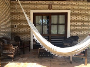 A hammock in a covered outdoor area with wicker furniture and a brick wall.