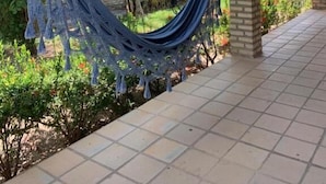 A covered outdoor area with a hammock, tiled flooring, and greenery. - Chalé no Condominio Porto do Sol (Tibau do Sul)