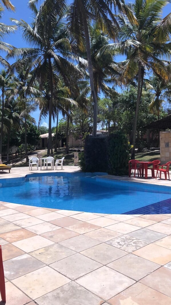 A swimming pool with tiled flooring, surrounded by palm trees and outdoor furniture.