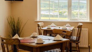 A dining area with a table set for four, a potted plant, and a view of the countryside through a window. - Seaview Heights (Dingle)
