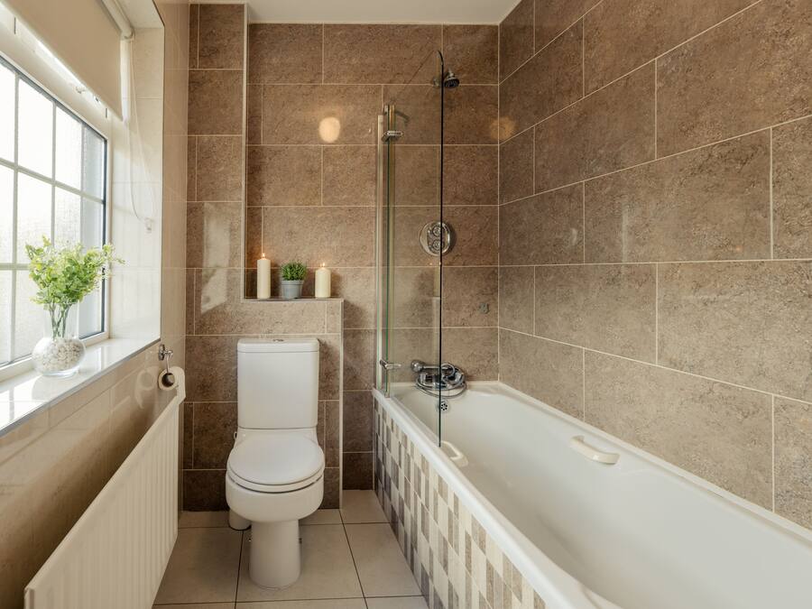 A bathroom with a toilet, bathtub, and a window with a plant.