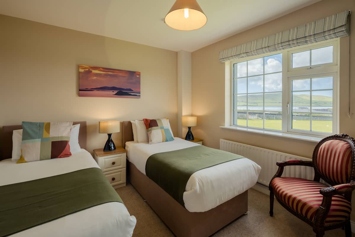Quarto de hotel com duas camas, vista para o campo e uma janela grande com cortinas.