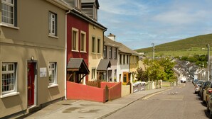 A row of townhouses with a red door, a sign indicating a service charge, and a clear view of the street. - Seaview Heights (Dingle)