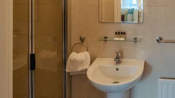 Un baño con cabina de ducha de vidrio, lavabo, espejo y perchero para toallas.