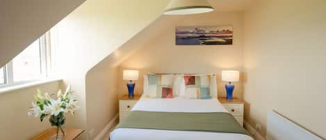 A bedroom with a bed, bedside tables, lamps, a painting, and a vase with flowers.