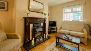 A living room with a fireplace, a sofa, a television, and a window with curtains. - Seaview Heights (Dingle)