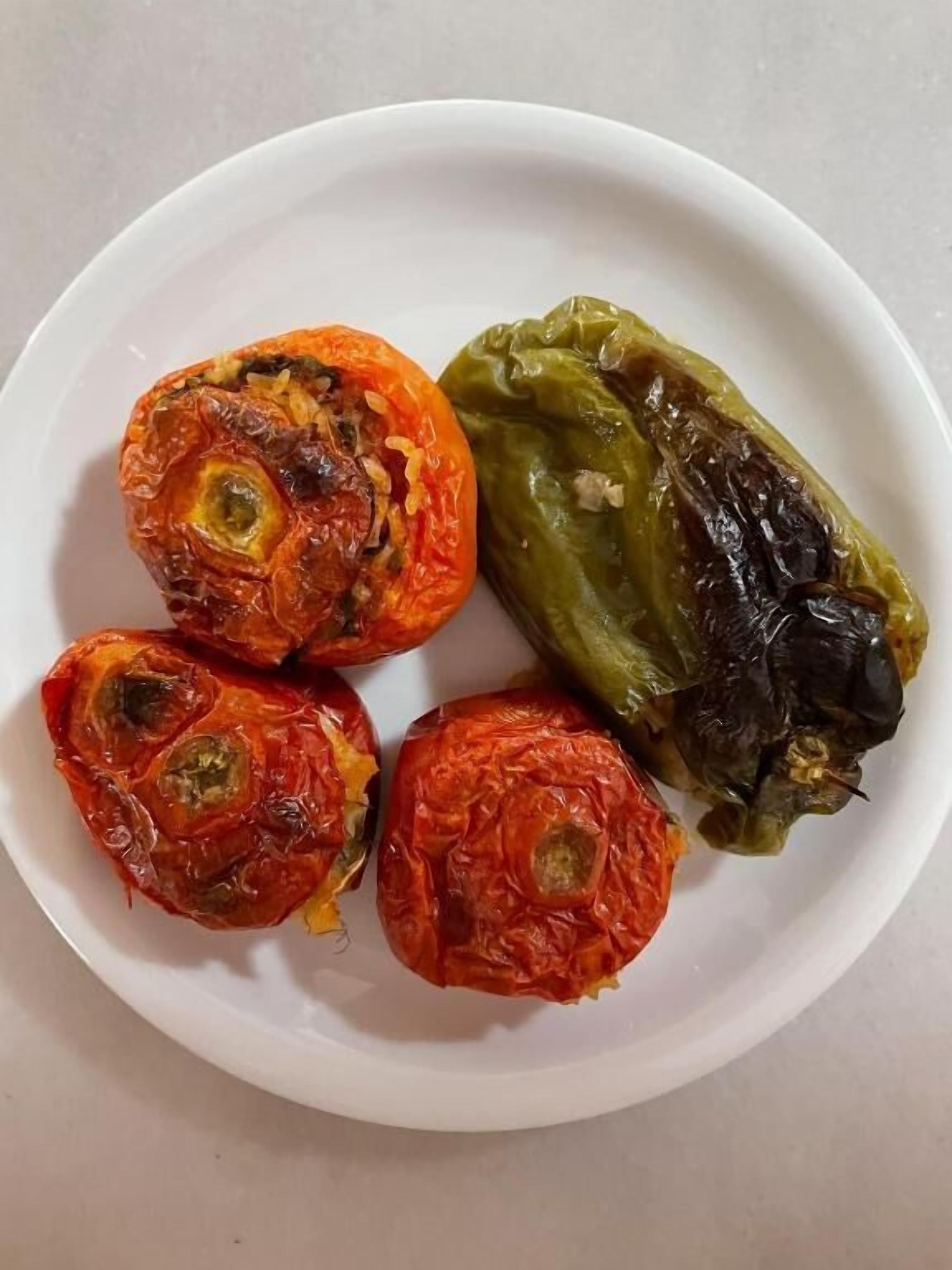 Un plato con cuatro pimientos rellenos, dos rojos y dos verdes, sobre un plato blanco.