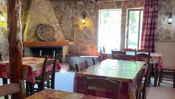 A dining area with stone walls, wooden beams, and tables covered with patterned tablecloths.