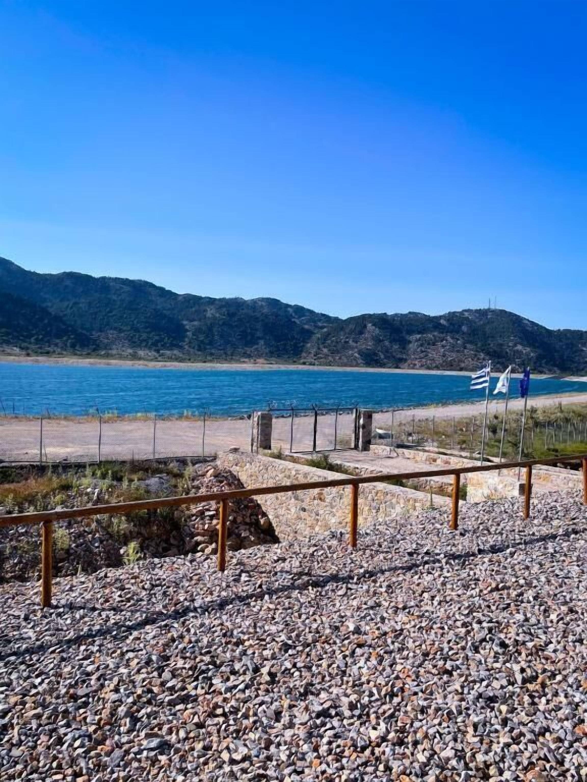 Zona de playa con arena de guijarros, una cerca de madera y un cartel.