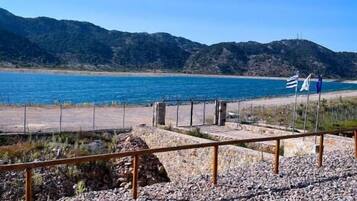 Zona de playa con arena de guijarros, una cerca de madera y un cartel.