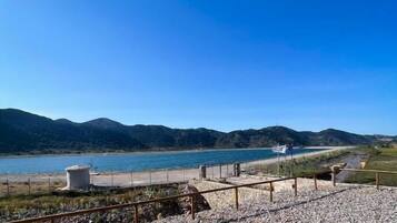 Ein Kiesstrand mit einer Umzäunung und freiem Blick auf das Wasser und ferne Berge.