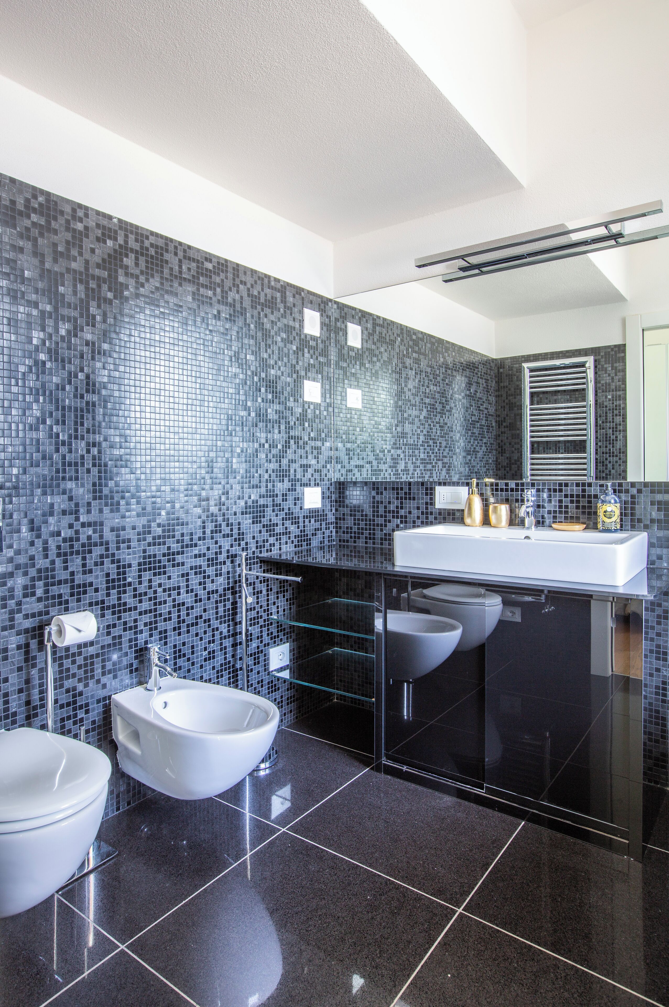 A modern bathroom with a black tiled wall, a white sink, and a bidet.