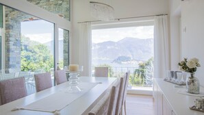 Un coin repas avec une table dressée pour quatre personnes, un lustre et une vue sur les montagnes et un lac.
