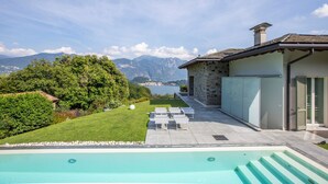 Un espace piscine avec des chaises longues, un bâtiment en pierre et une vue sur les montagnes et un lac.