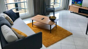 Ett modernt vardagsrum med en soffa, ett soffbord, en tv och utsikt över staden genom stora fönster.
