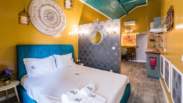 Hotelkamer met een groot bed, een blauw hoofdbord, een decoratief wandbord en een kleintje tafeltje met een plant.