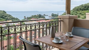 A balcony with a table set for two, overlooking a coastal view with buildings and greenery. - Enetiko Resort Hotel (Parga)