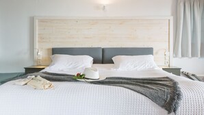 A neatly made bed with a white quilt, a gray throw blanket, and a white hat with a red flower. - Enetiko Resort Hotel (Parga)