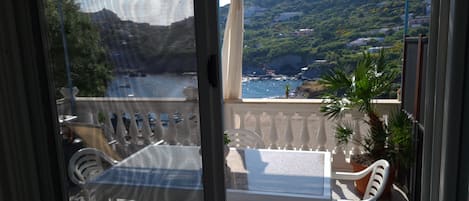 Een balkon met een tafel en stoelen, met uitzicht op een kustlandschap met kliffen en de zee.