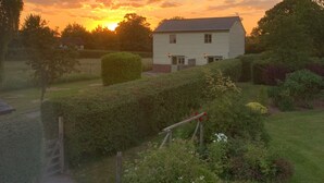 A house with a well-maintained garden and a clear view of the sunset in the background. - Orchard Cottage. 2-bedroomed cottage. Short breaks welcome. Free Wi-Fi (Hereford)