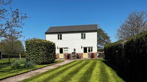 A two-story white building with green doors and windows, surrounded by a well-maintained lawn and hedges. - Orchard Cottage. 2-bedroomed cottage. Short breaks welcome. Free Wi-Fi (Hereford)