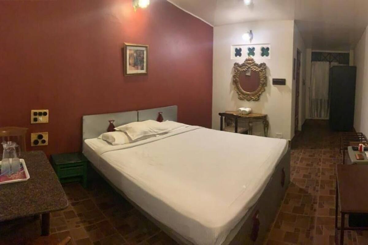 Un dormitorio con cama, una mesita, una silla, un espejo y una puerta que da a otra habitación.