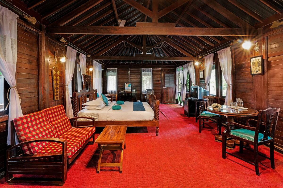 Habitación acogedora con techo de madera, cama, sofá, mesa de comedor con sillas y alfombra roja.