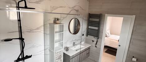 A modern bathroom with a glass-enclosed shower, a vanity with a mirror, and a walk-in closet.