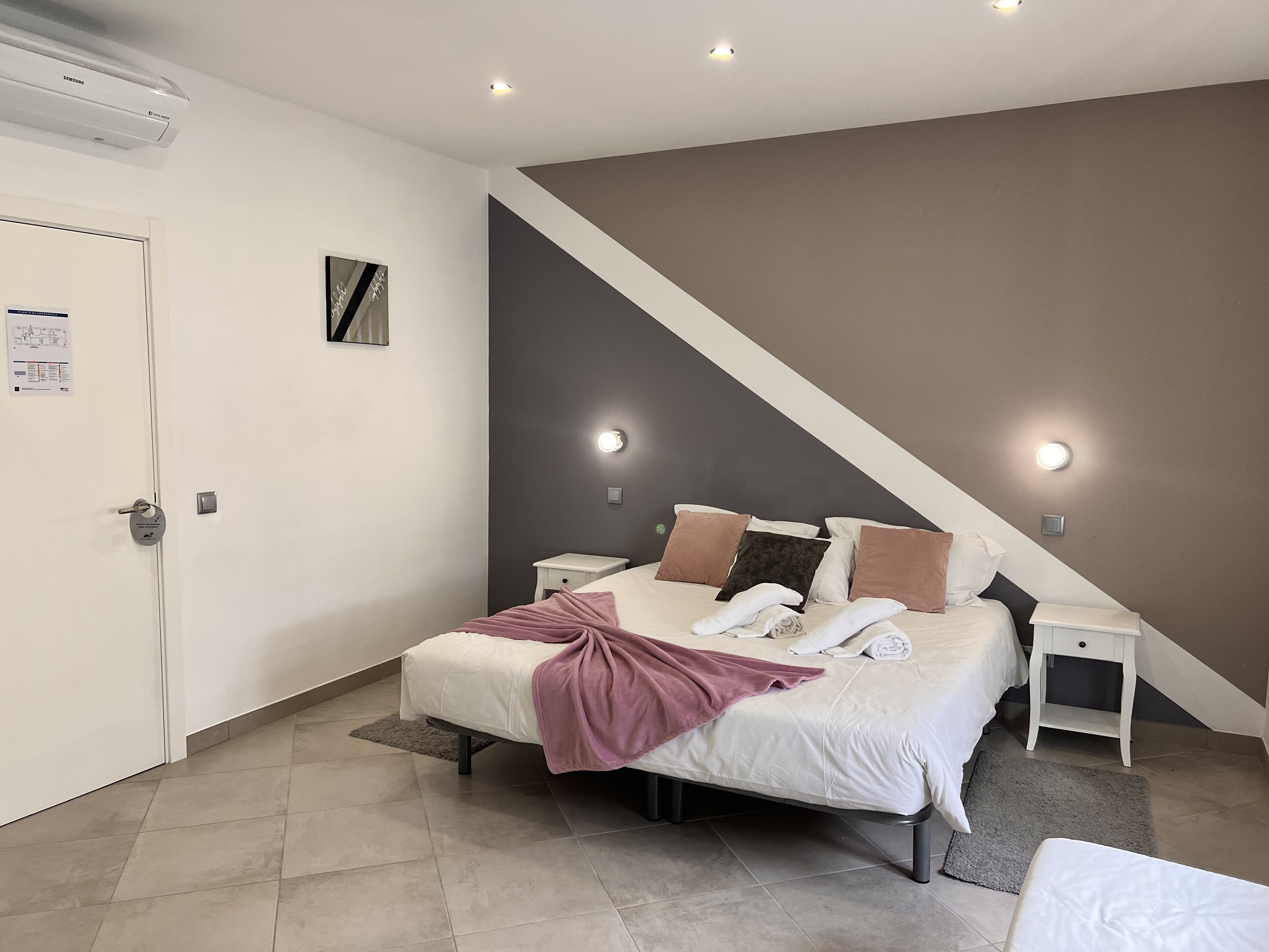 Un dormitorio con cama, mesitas de noche, aire acondicionado instalado en la pared y una puerta con cerradura.