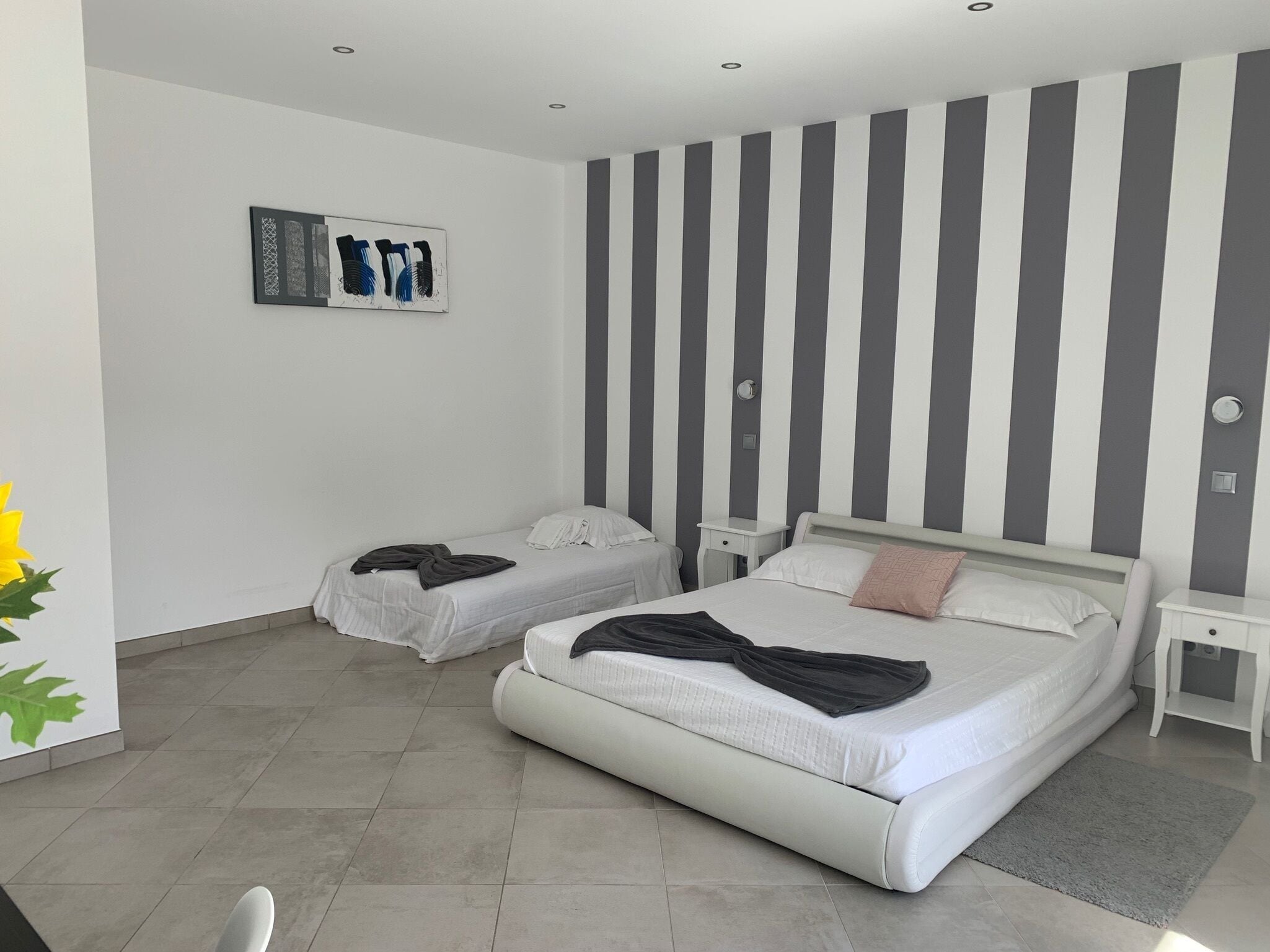 A modern bedroom with two beds, striped wallpaper, and a small bedside table.