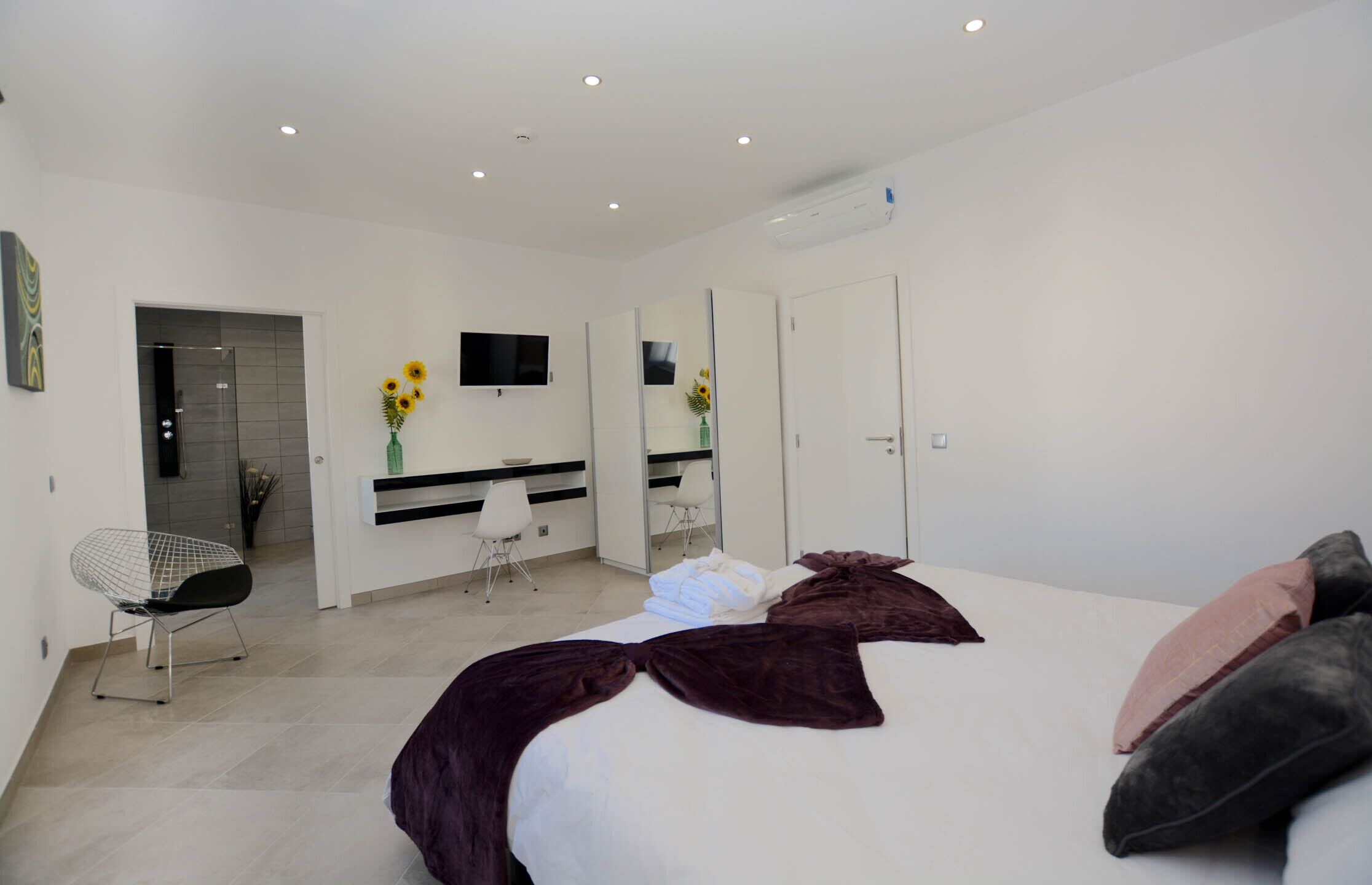 A modern bedroom with a large bed, a desk, a chair, and a TV.
