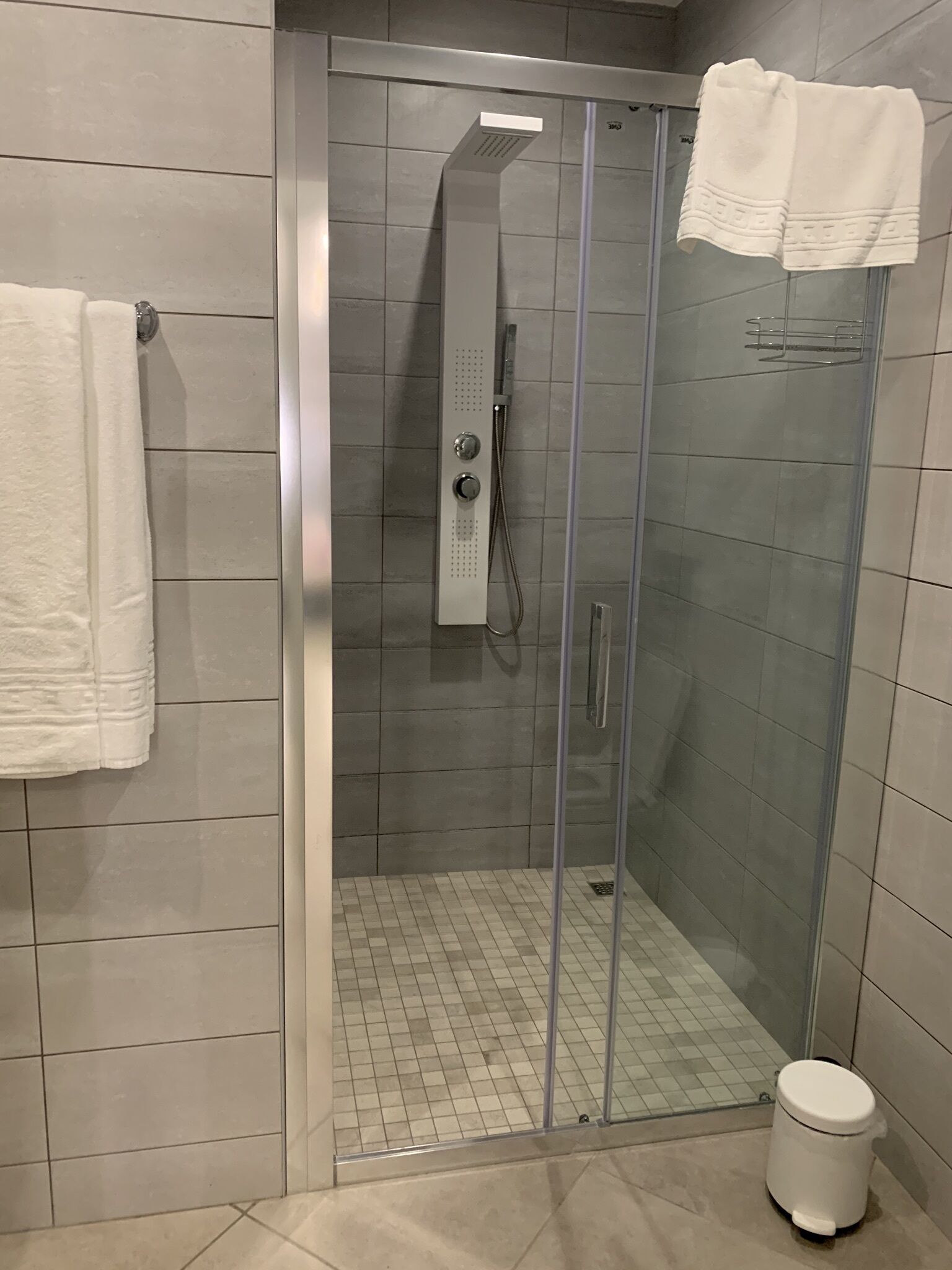 Eine moderne Duschkabine mit Glastür, einer Handbrause und einem weißen Handtuch an der Wand.