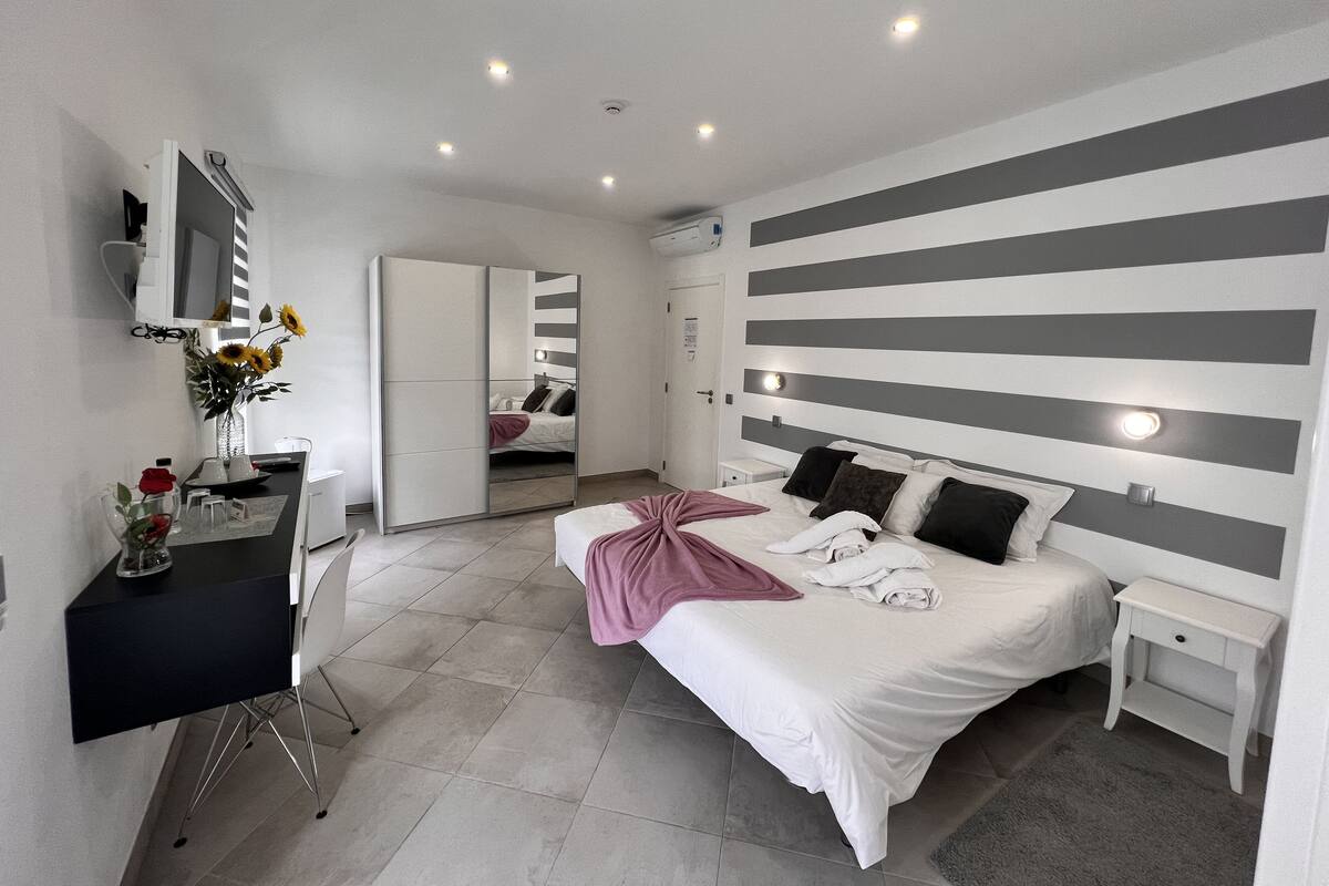 A modern bedroom with a bed, bedside tables, a desk, and a mirror.