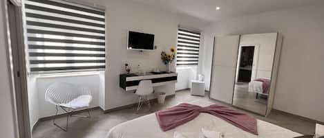 A modern bedroom with a bed, a desk, a chair, a TV, and a mirror.