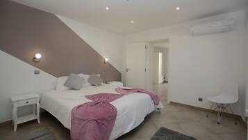 A bedroom with a bed, bedside tables, a chair, and an air conditioning unit.