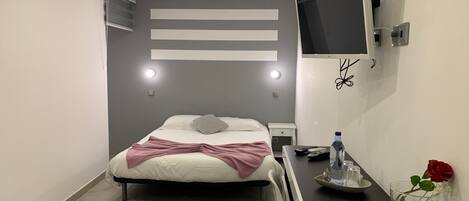 Ein modernes Hotelzimmer mit Bett, Nachttisch, Fernseher und einer Vase mit einer Rose.