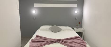 A modern bedroom with a bed, bedside tables, and wall-mounted lights.