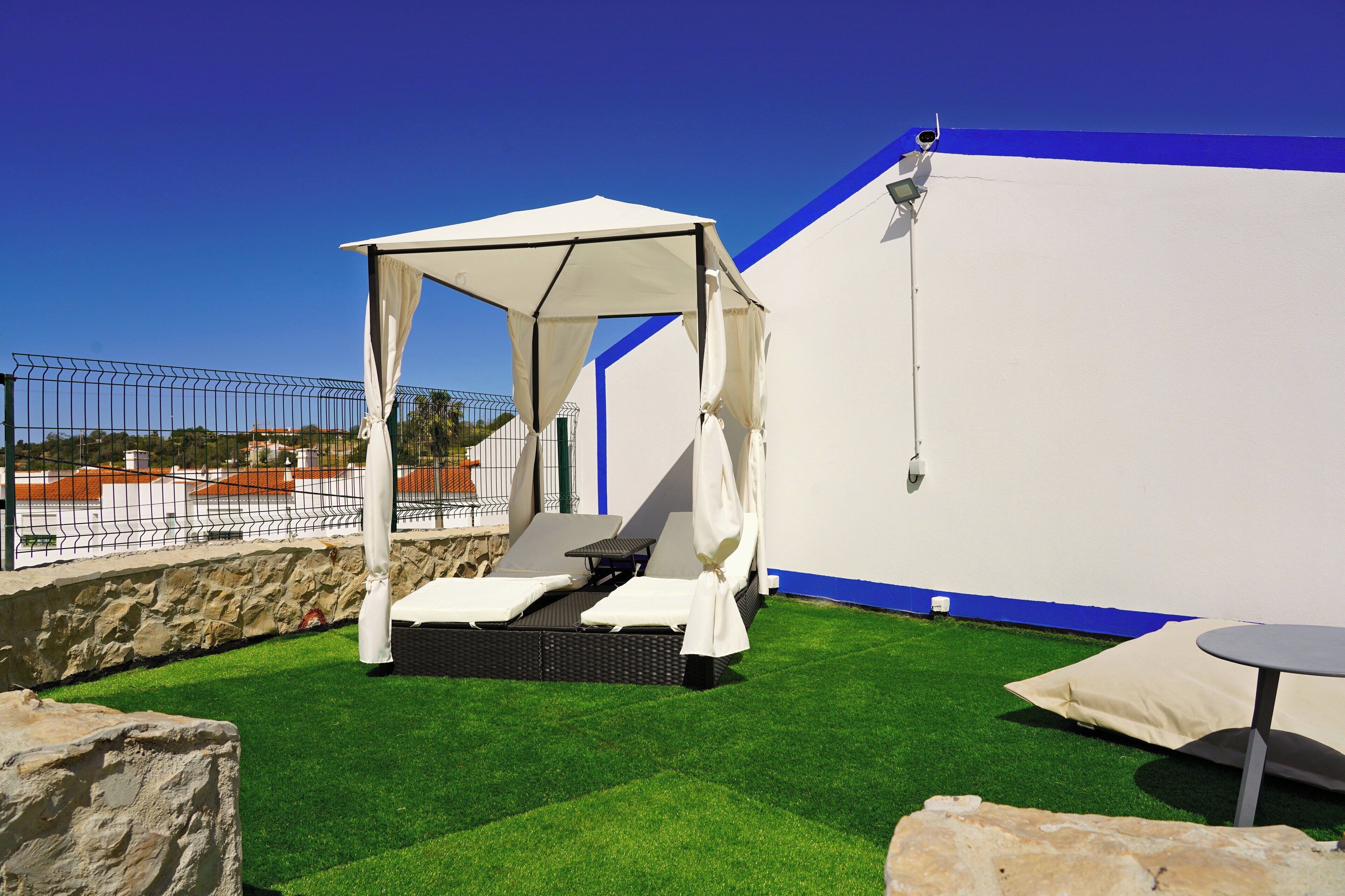 A rooftop terrace with a white canopy bed, a small table, and a stone wall.
