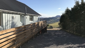 A building with a sloped roof and a gravel driveway leading to a wooden fence. - Stylish, spacious lodge with panoramic views, an ideal base for Loch Ness (Drumnadrochit)