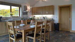 A modern kitchen with wooden cabinets, a dining table with chairs, and a view of trees outside. - Stylish, spacious lodge with panoramic views, an ideal base for Loch Ness (Drumnadrochit)
