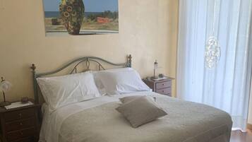 A bedroom with a bed, a nightstand, a lamp, a decorative vase on the wall, and a window with curtains.