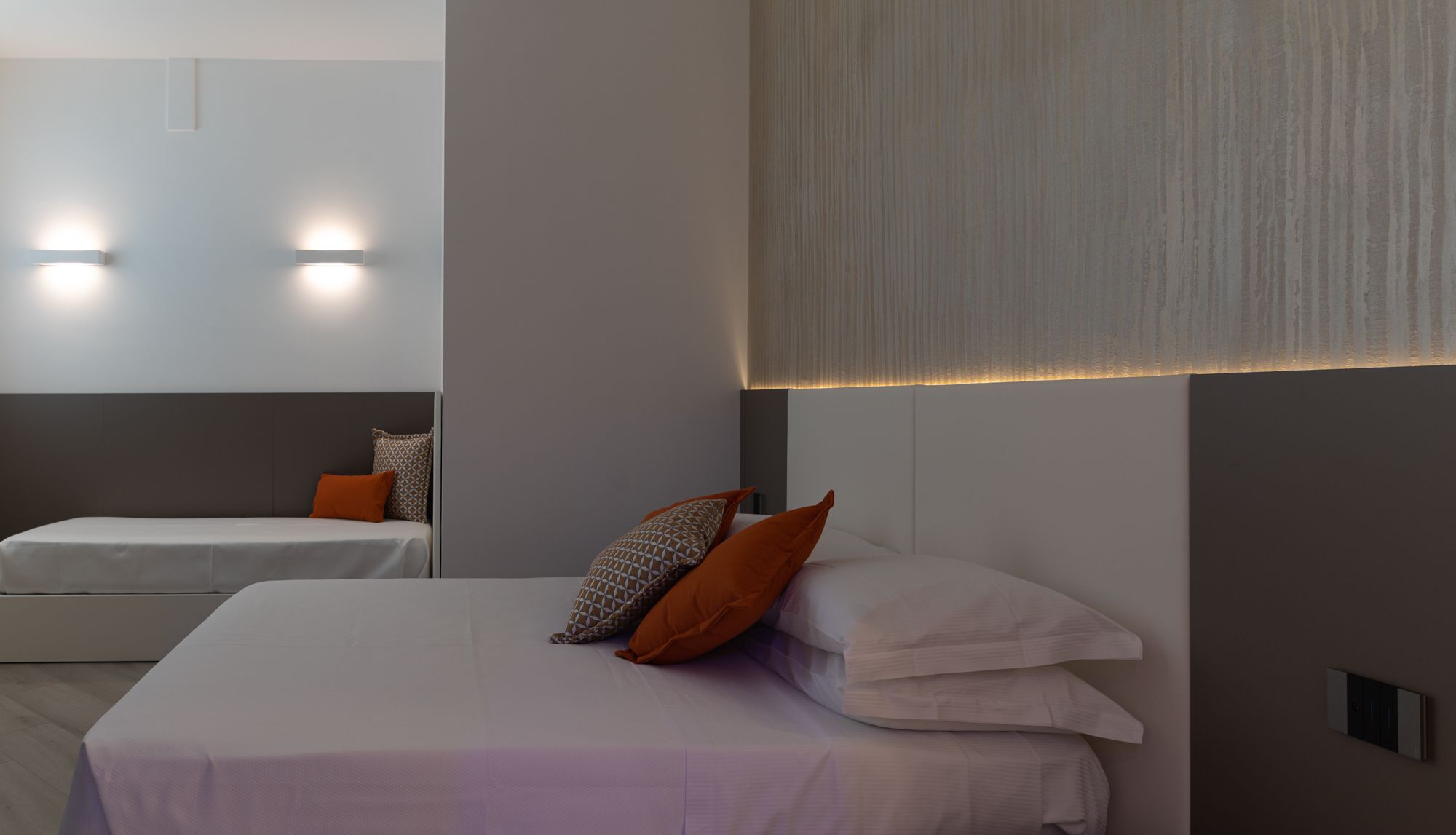 Une chambre d’hôtel moderne avec un grand lit, un lit plus petit et deux lampes fixées au mur.