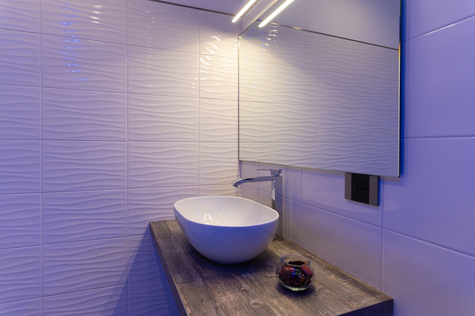 A modern bathroom with a white textured wall, a large white sink, and a wooden countertop.