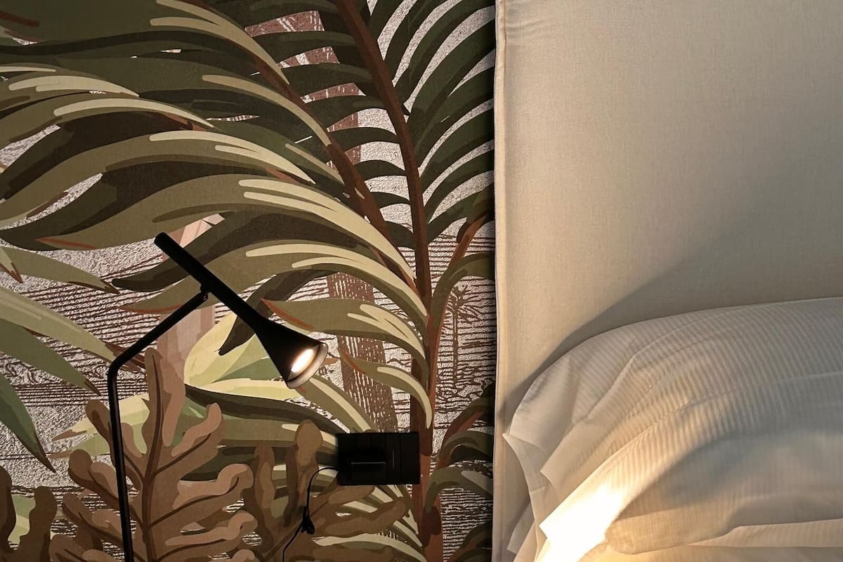 A bed with white linens and a wall with a leaf-patterned design.