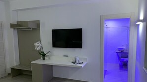 Une chambre moderne avec un téléviseur à écran plat fixé au mur, une petite console blanche et une orchidée en pot.