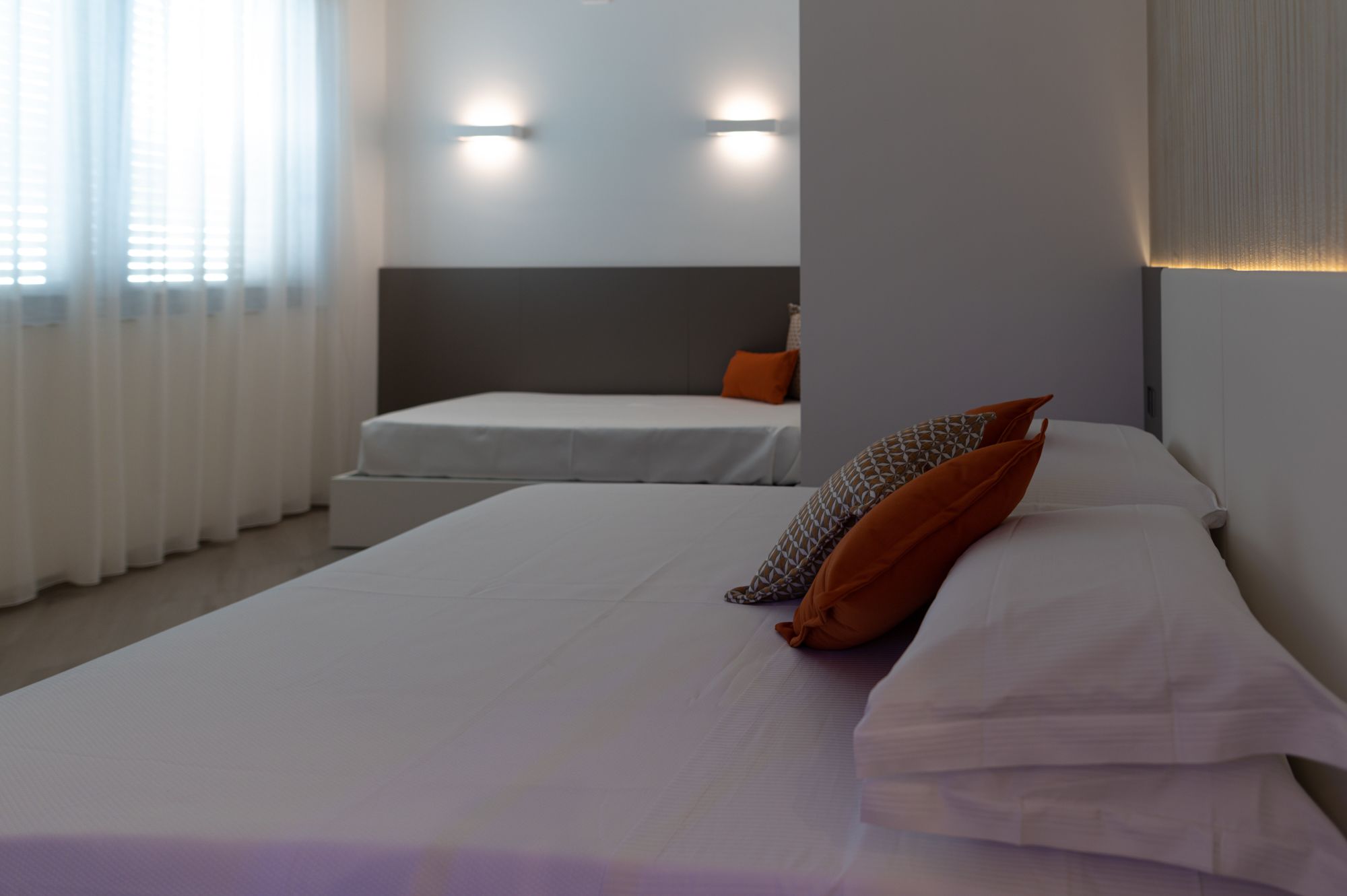 A hotel room with a large bed, a smaller bed, and two wall-mounted lights.