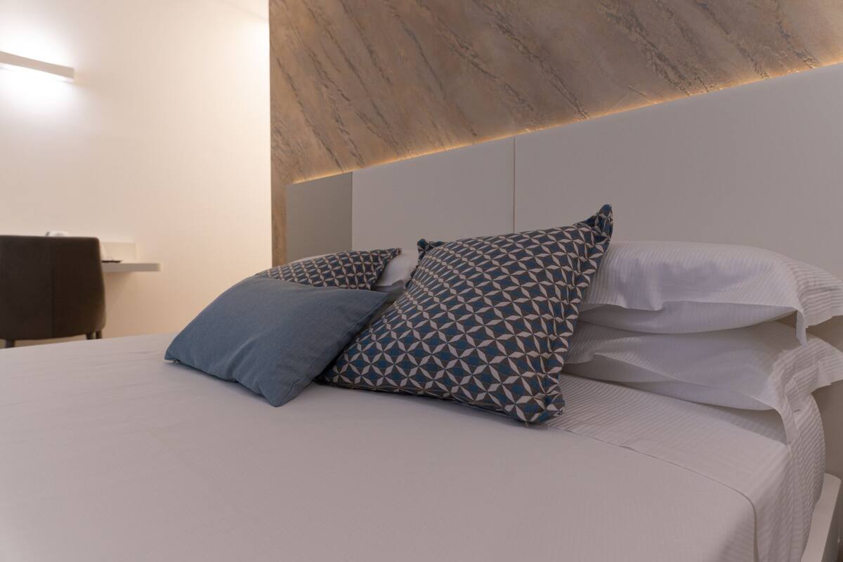 A neatly made bed with patterned pillows and a plain white headboard.