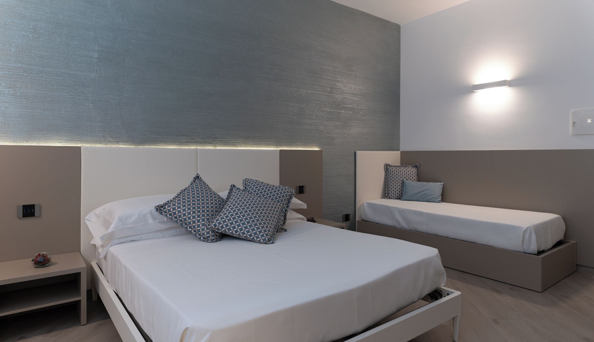 A modern bedroom with a large bed, a smaller bed, and a nightstand.