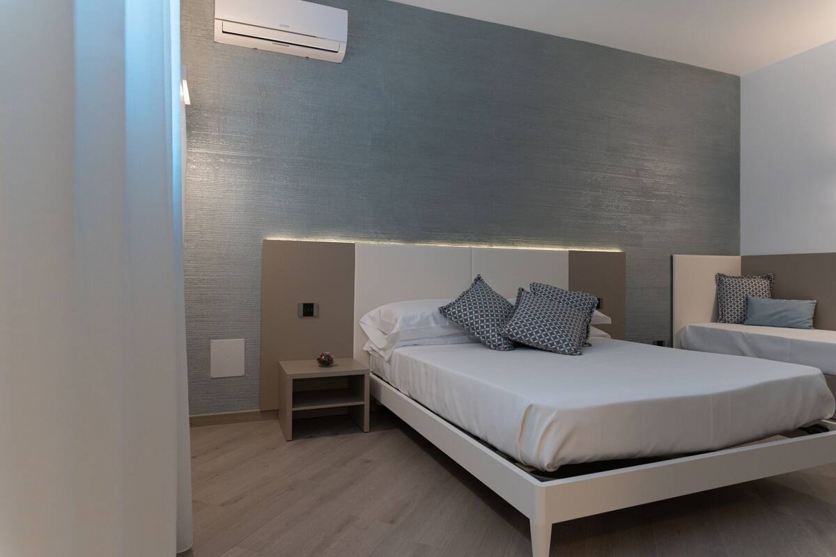 A modern bedroom with a bed, bedside tables, and a wall-mounted air conditioner.